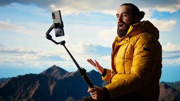 Traveler filming his hiking experience in the wilderness documenting his adventure on social media using his smartphone. Recording the beautiful scenic mountain view behind him for content. Camera A. photo