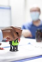 Closeup of african american doctor stamping a clipboard as elderly male patient with face mask waits at desk. Black general practitioner completing senior man prescription with a stamp. photo