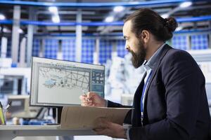 Inspectors in photovoltaics factory reviewing performance of solar panels assembly lines, reading paperwork. Supervisor inspecting solar plant machinery, looking over documentation files photo
