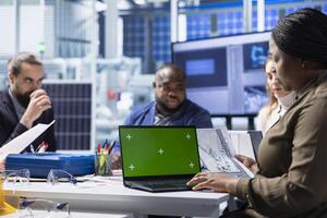 Factory management team look over schematics, planning work using isolated screen laptop. Solar panels plant shareholders look over assembly lines blueprints diagrams, working on mockup notebook photo