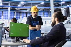 Photovoltaics factory manager using green screen PC to show worker how to optimize production flow. Sustainable energy solar panels plant supervisor monitors manufacturing process on mockup computer photo