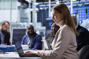 Photovoltaics factory management team analyzing data using laptop, reviewing system health metrics. Solar panels manufacturing plant executives troubleshooting technical issues using notebook photo