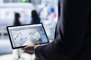 Technician in solar panel facility reviewing photovoltaic system performance on tablet. Close up of specialist analyzing production metrics on device to optimize efficiency in industrial plant photo