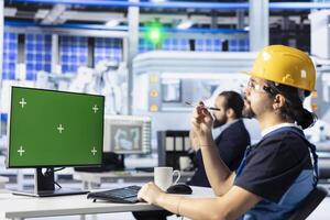 Technician uses green screen PC to monitor solar panel manufacturing plant assembly lines. Worker uses chroma key computer to troubleshoot photovoltaic equipment, ensuring seamless production workflow photo