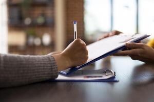 Closeup of an individual signing a document, completing recruitment process in startup company. Selective focus of a person holding a pen and writing on a clipboard at an office desk. photo