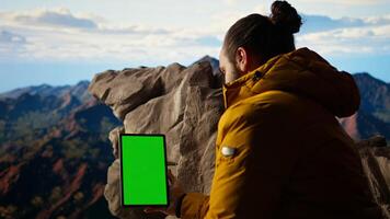 Mountaineer stands at the peak with satisfaction and uses mockup screen, hiker admires breathtaking view with crisp air on mountain top. Scenic surroundings highlights determination. Camera A. photo