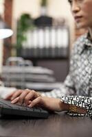 Female professional typing on computer keyboard at a modern office desk. Asian woman busy inputting project details, touching keys to update company financial information on the desktop pc. photo