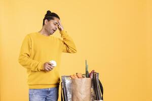 Exhausted deliveryman suffering headache while taking takeaway order out of bag. Tired man holding coffee cup, taking groceries order out of thermal backpack ordered by customer, studio background photo
