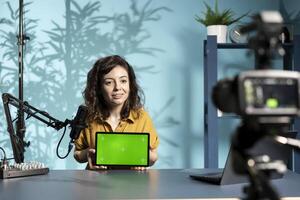 Happy influencer in studio filming mockup tablet review for tech enthusiasts. Joyful media star hosts technology internet show, unboxing isolated screen digital portable device photo