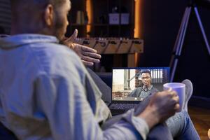 African american web user meeting with workmates on a call remotely, ensuring a strong discussion via wireless connection. Freelancer joining an executive conference from his loft photo