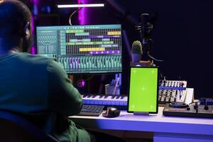 Young musician mixing and mastering songs next to isolated mockup display, operating on digital audio software to add sound effects on new tracks recorded. Audio engineer in home studio. photo