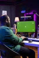 Audio engineer producing new music on display with greenscreen, working on mixing and mastering tracks in his home studio. Skilled artist having fun editing tunes on stereo console. photo