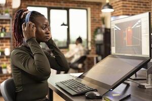 African American designer refining projects on digital monitors enhancing visuals in modern creative workspace. Black woman focused on editing and 3D modeling working across multiple screens. photo