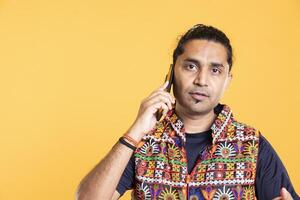 Portrait of indian man discussing with best friend over telephone call using smartphone. Cheerful person talking with mate in phone call using cellphone, isolated over studio background photo