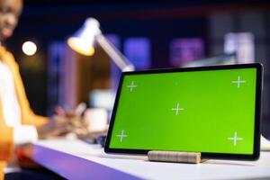 Focus on green screen tablet used by employee in blurry background checking emails, reading messages in inbox. Close up of mockup tablet used by freelancer sorting electronic correspondence photo