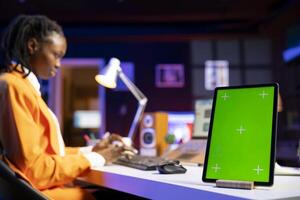 Woman working from home on notebook, using green screen device to write notes. Remote worker in personal apartment office using laptop, transcribing important info on mockup tablet photo