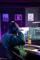 Musician playing piano keys and editing to improve the sound quality of audio recordings in his home studio, putting on headset. Music producer uses midi controller to manipulate sounds. photo