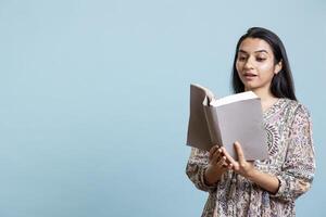 Positive jolly woman reading interesting book and enjoying lecture hobby, being entertained against studio background. Indian relaxed person with intriguing novel in arms enjoys free time. photo