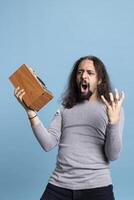 Energetic musician with long hair striking a rock and roll pose in the studio, listening to dynamic music on a loud speaker. Showing enthusiasm and joy for the essence of rock performance. photo