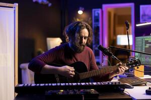 Musician with condenser microphone creating a song on guitar, working on mixing and mastering tunes. Artist audio engineer recording music and adding sound effects in post production, acoustics. photo