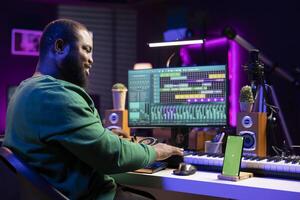 Composer musician mixing his tracks in pc software with an isolated smartphone screen, working on launching new music. Artist operating on mixing console, producing and editing sounds. photo