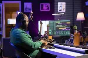 African american music producer counting down before starting a recording session, operating on mixing console and professional editing software. Sound engineer producing songs in home studio. photo