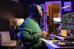 Young producer performing a live acoustic song in home studio, recording a new track on microphone and using DAW software. Artist songwriter editing the audio files in post production. photo