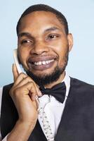 Smiling bellboy assisting guests to find lodging on landline phone call, providing important information about hotel amenities. Professional doorman on the telephone discussion. photo