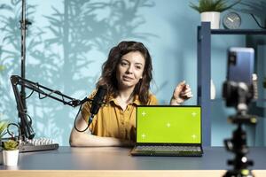 Smiling tech guru in studio filming tech tutorial on how to do maintenance on mockup laptop. Happy internet show host teaching viewers how to open and repair damaged isolated screen notebook photo