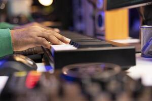Musician producer hitting notes on piano electronic keyboard, editing his music in post production with mixing console. Artist composing songs with sounds from synthesizer midi controller. Close up, photo