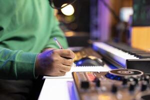 Songwriter taking notes on paper to compose a new soundtrack, making rhymes and mixing musical elements together. Artist composer creating new verses for a song in home studio. Close up. photo