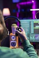 Music producer using his headphones for a mix and master session, adding sound effects and adjusting volume levels on mixing console and amplifier. Digital audio software to edit tracks. Close up. photo