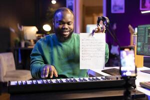 Musician songwriter presents notes on music sheet and demonstrating on piano, hosting online master class acoustics lessons. Composer teaching people to play electronic keyboard synthesizer. photo
