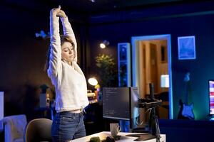 Computer scientist doing software quality assurance, stretching after reading source code, feeling tired. IT staff member relaxing muscles after inspecting coding to fix potential issues all day photo