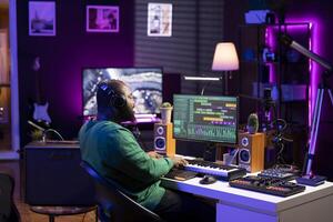 Audio producer playing piano electronic synthesizer to create a new tune, adjusting volume levels on old recordings. Music engineer recording sounds, plays tracks on midi controller. photo