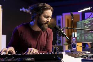 Music producer plays electronic piano keyboard notes and singing on microphone, creating audio recordings before launching music. Artist uses synthesizer and amplifier, post production. photo