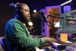 Young artist playing piano keys and singing song on microphone, composing his new music and mixing the tracks on digital interface. Producer technician composing melody with gear. photo