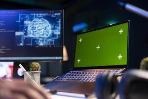 Black person programming neural network code with a green screen on computer to build databases. System engineer working from home while looking at data center security servers. photo