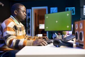 Black web developer handling database servers for safety with green screen, writing code on terminal window next to isolated chroma key. Programming language for machine learning. photo