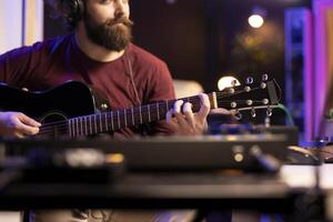 Musician playing guitar and uses mixing gear to create new music, looking at daw software interface on computer. Producer recording soundtracks with electronic equipment, acoustical engineering. photo