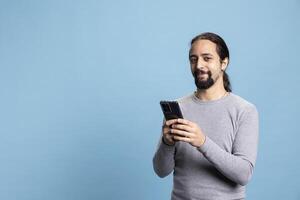 Professional young man in casual clothes using a phone with a pensive expression, embodying the modern digital professionalism. Cool male model uses device on blue background. photo