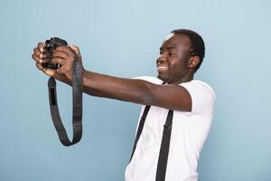 Black male photographer taking a snapshot of himself, holding his camera with the lens facing him. Young man smiling confidently and standing with a dslr against an isolated background. photo