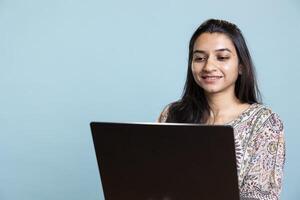 Successful casual copywriter typing on her laptop in front of camera, focused on her work and freelancing tasks. Young smiling person working on her wireless computer, remote job. photo