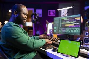Skilled songwriter producing new music on audio software, having a greenscreen next to him. Musician using mixing and mastering techniques with stereo gear to improve his tracks. photo