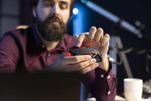 Influencer filming review for online channel in apartment studio, testing gaming mouse for audience. Man rotating wheel on computer peripheral device, checking for flaws photo