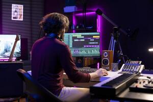 Sound engineer working in his home studio with daw software on computer and mixing tools, creating music. Producer mixing and mastering soundtracks, signal processing acoustical engineering. photo
