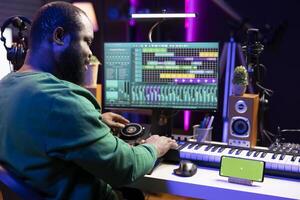 Male composer using mixing console and piano to edit tracks, having a greenscreen on smartphone. Musician producing new songs with mixing and mastering techniques in home studio. photo