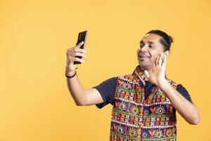 Cheerful man doing waving hand gesture, chatting with friend over online videocall on smartphone. Jolly person greeting mate on teleconference using mobile phone, studio background photo