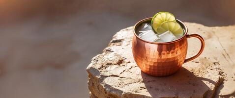 Refreshing copper mug filled with ice and lime slices on a rustic stone surface in warm sunlight photo