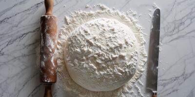 Dough ball covered flour with wooden rolling pin on white marble surface top view. photo